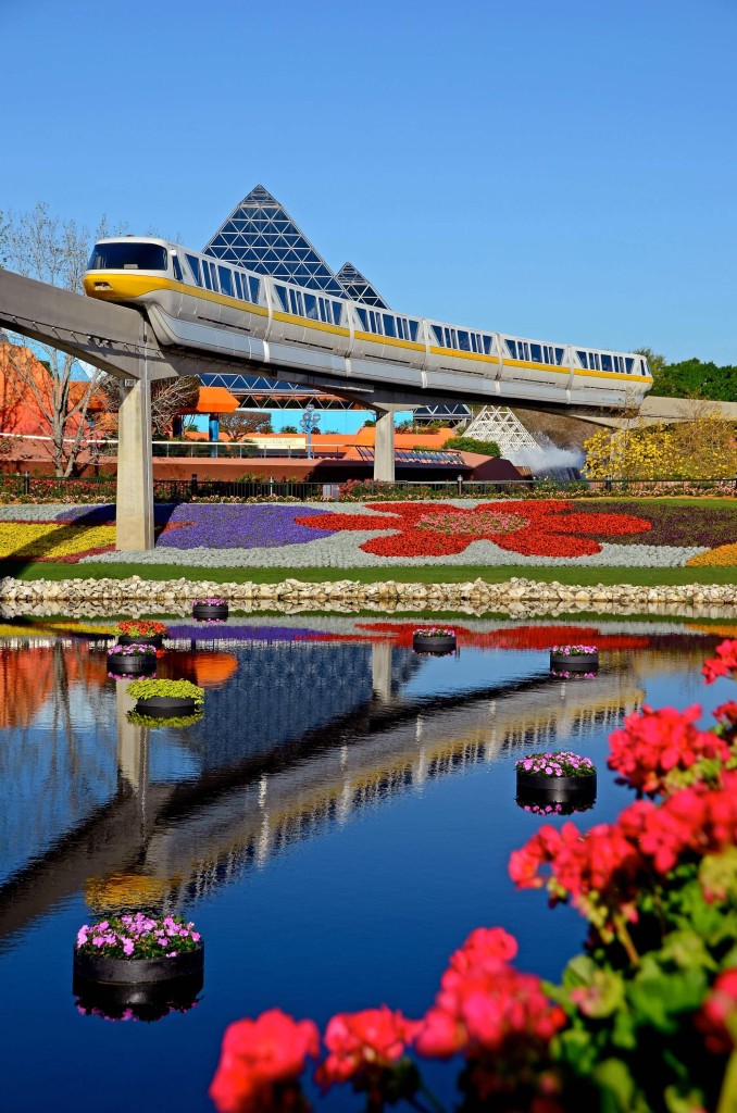 A photo of the monorail in Epcot with a beautiful display of gardens below.