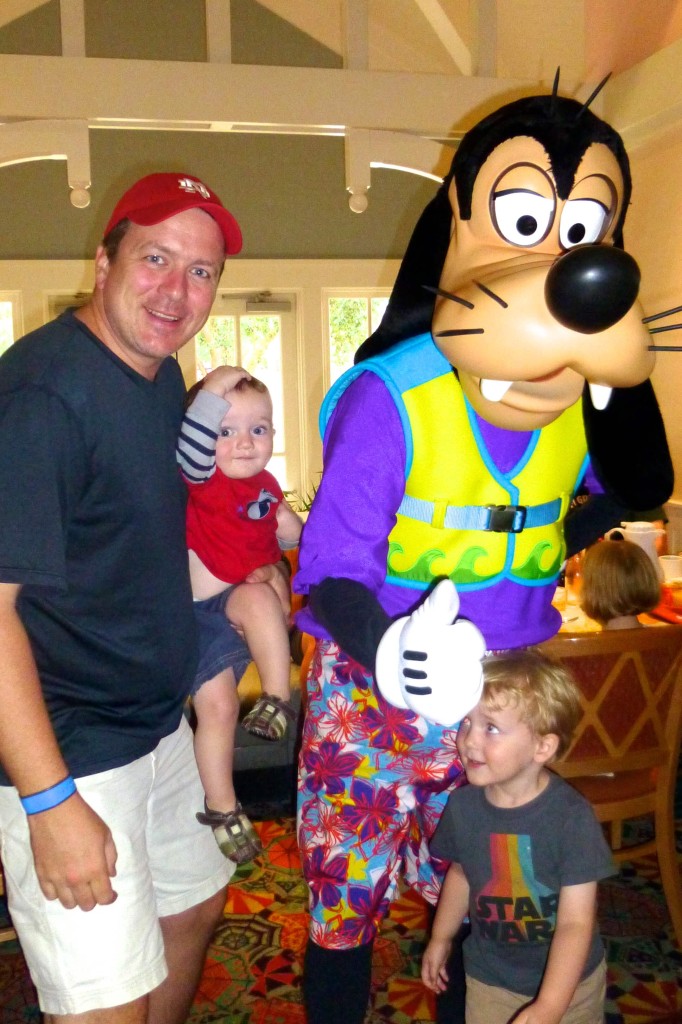 Goofy dressed in beach ware with a father and 2 little boys