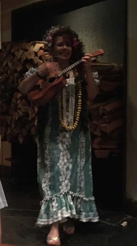 Woman dressed in traditional Hawaiian dress strumming a ukelele
